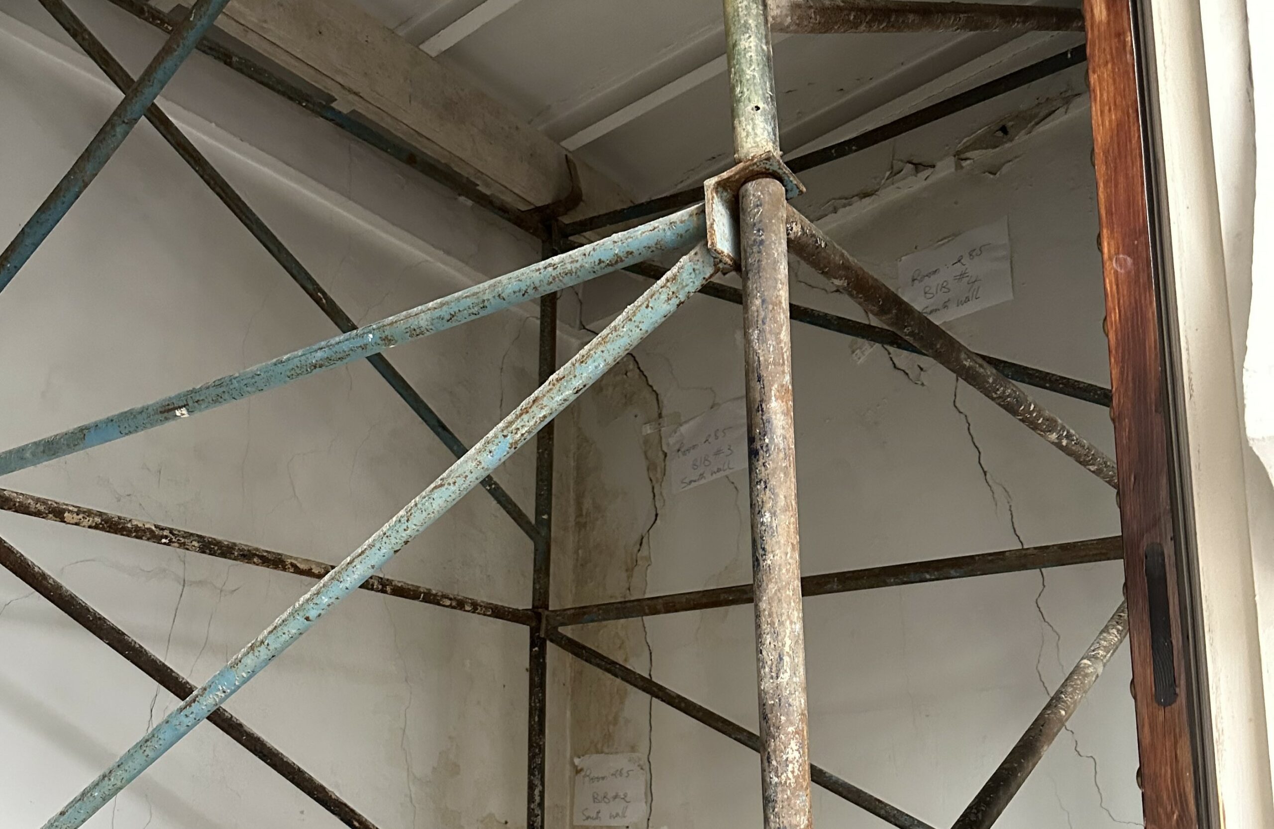 Scaffolding inside a room with plaster walls with large cracks.