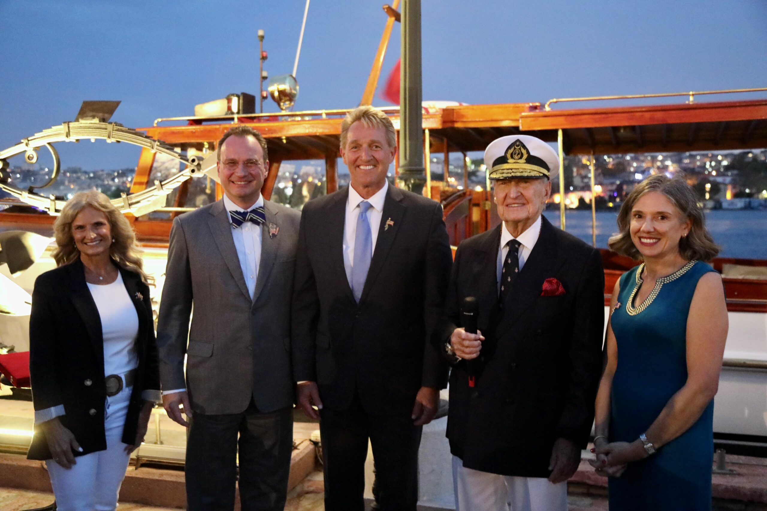 Group of people standing in front of a historic vessel at an evening event.